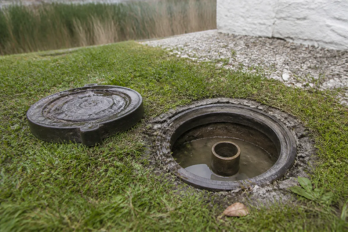 Regard de compteur d’eau ouvert dans une pelouse d’argile au bord d’un chemin de polder