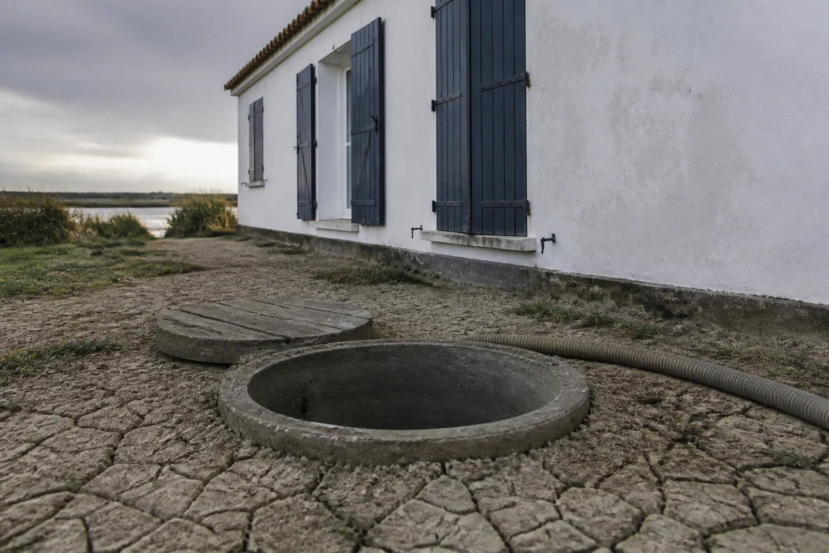 Regard d&rsquo;évacuation ouvert au pied d&rsquo;une maison basse blanchie du marais breton vendéen, roseaux en arrière-plan